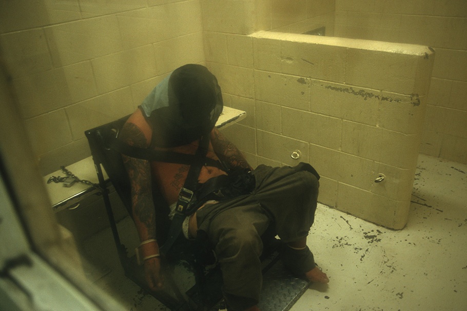 A man restrained to a chair with his head covered.