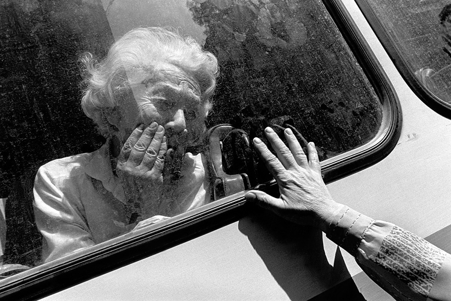 An elderly woman viewed through a vehicle window. 