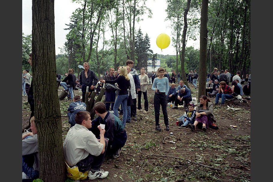A crowd of people in a park. One girl holds a yellow balloon.