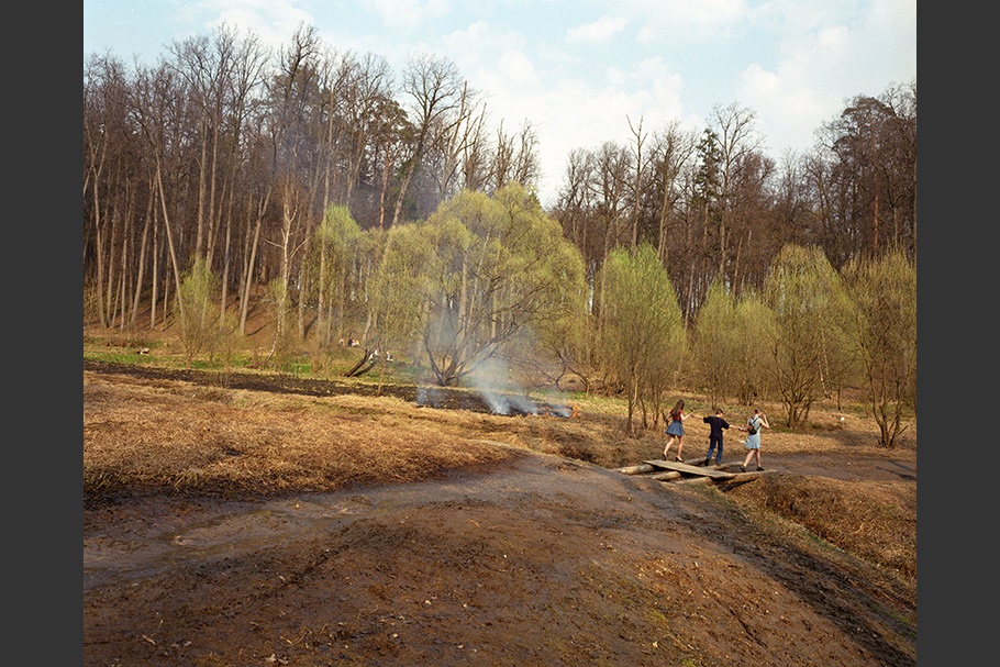 Three people walk in a park next to fires. 
