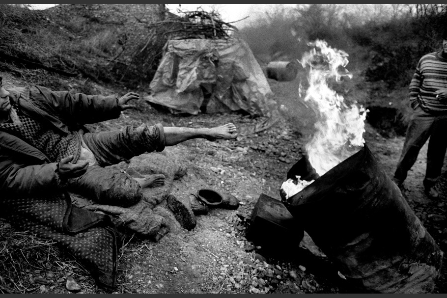 A man warms his feet by a fire in a barrel. 