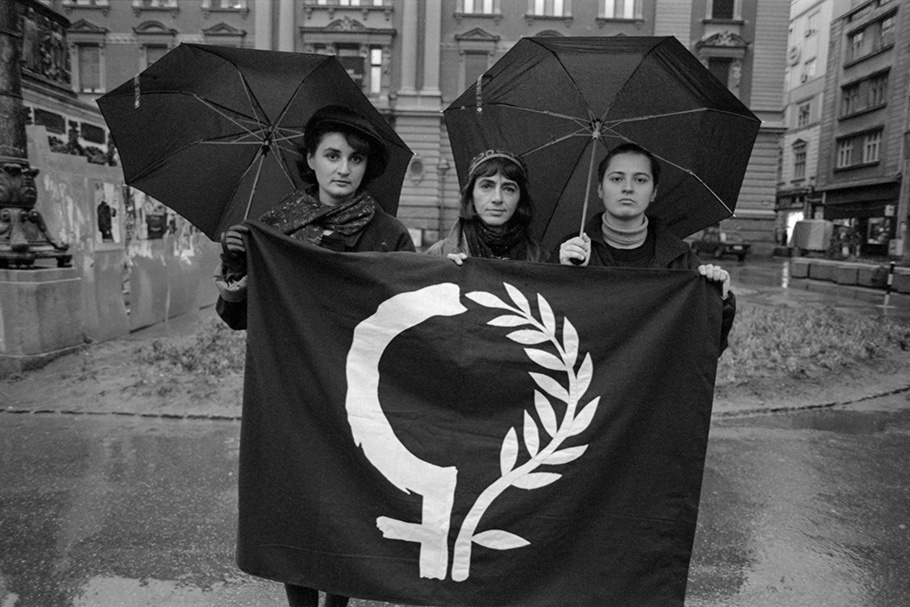 Three women holding a banner and umbrellas.