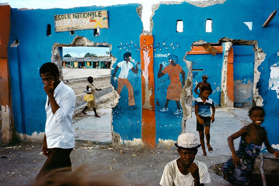 Children in front of a blue run down school wall with murals. 