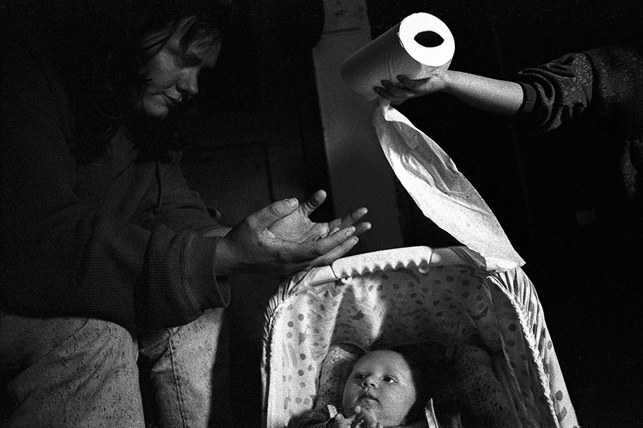 Hands passing a roll of toilet paper over a baby.