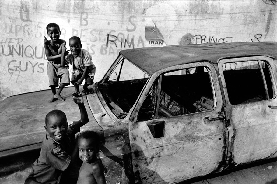Kids playing on a burnt out car.