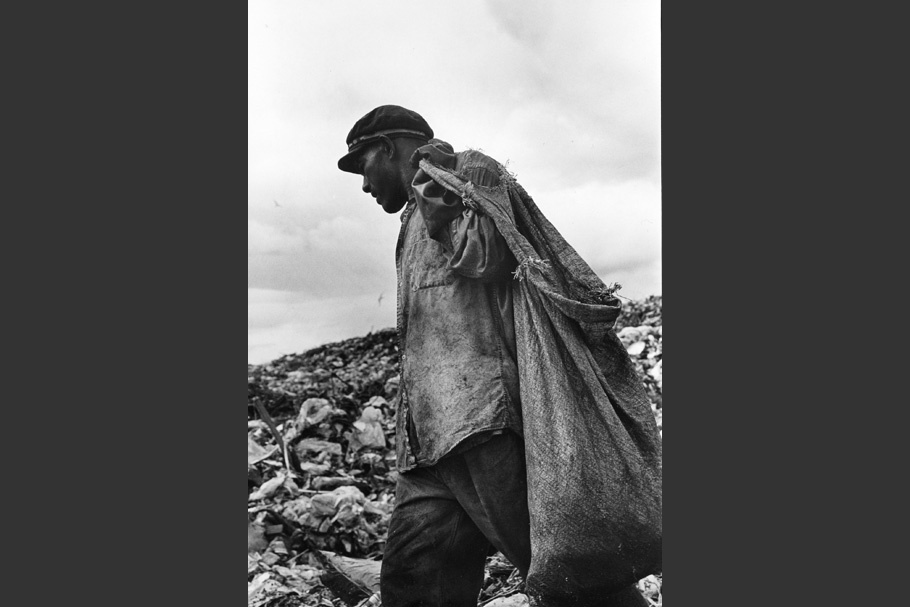 A man carrying a sack in a garbage dump.