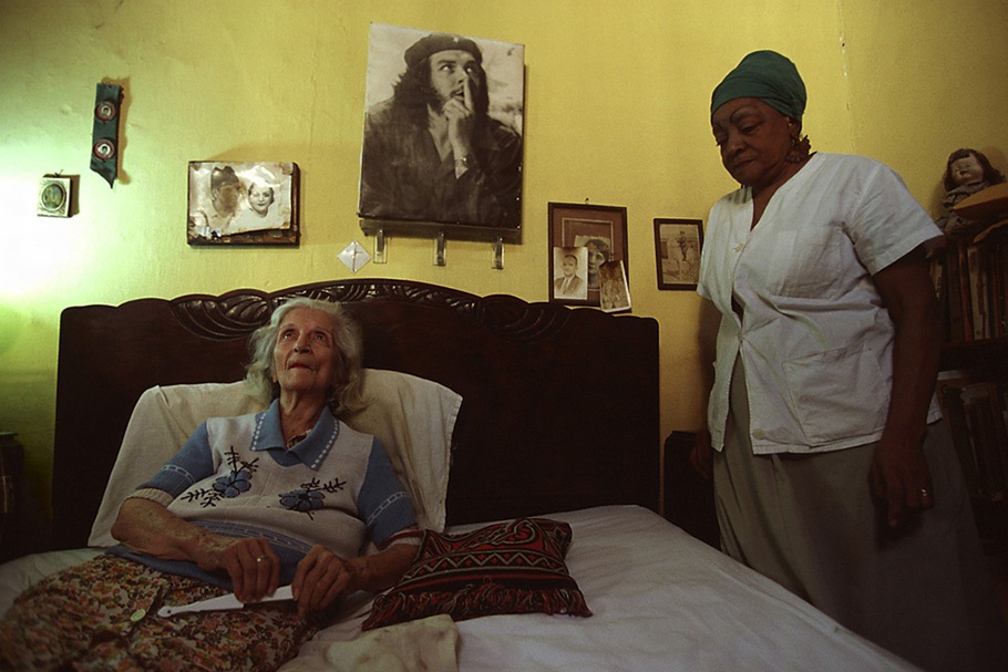 An elderly woman in bed with her caregiver nearby. 