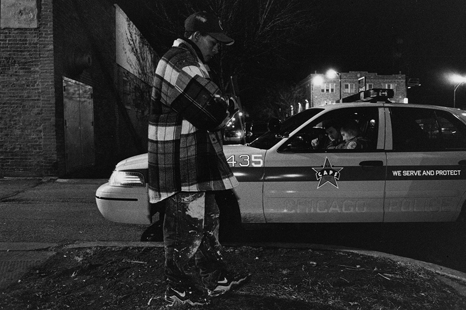 A man walking by a police car at night.