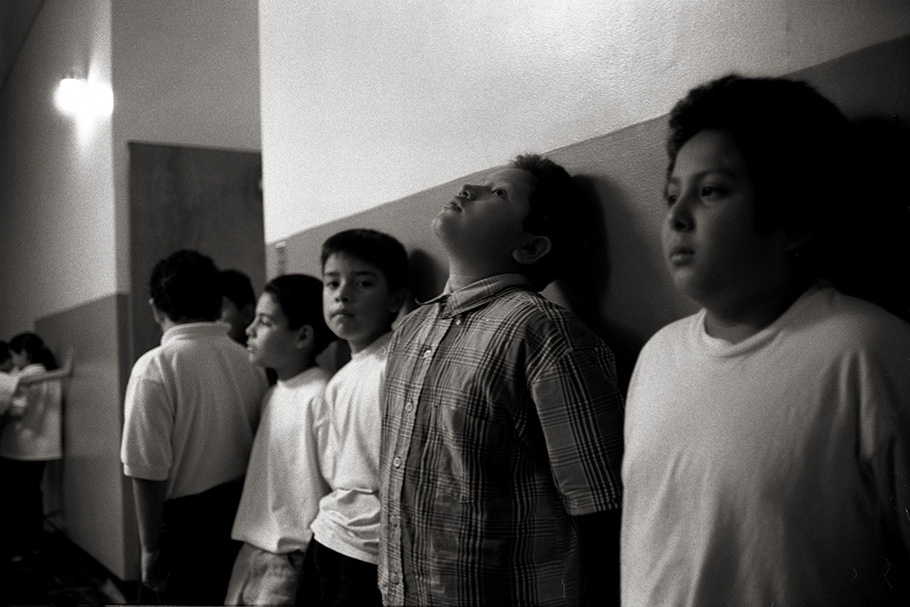 Boys lined up against a school hallway wall.