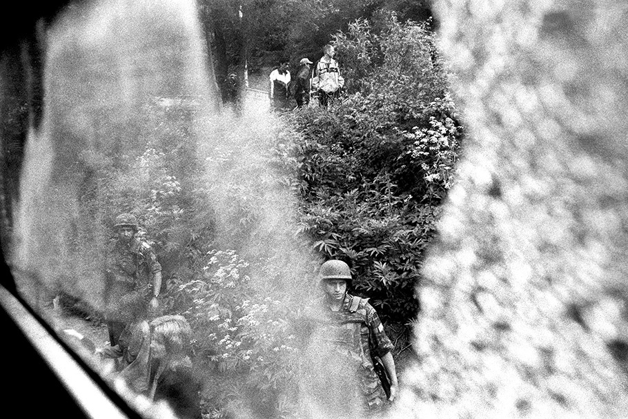 Soldiers and civilians viewed through train window with reflections.