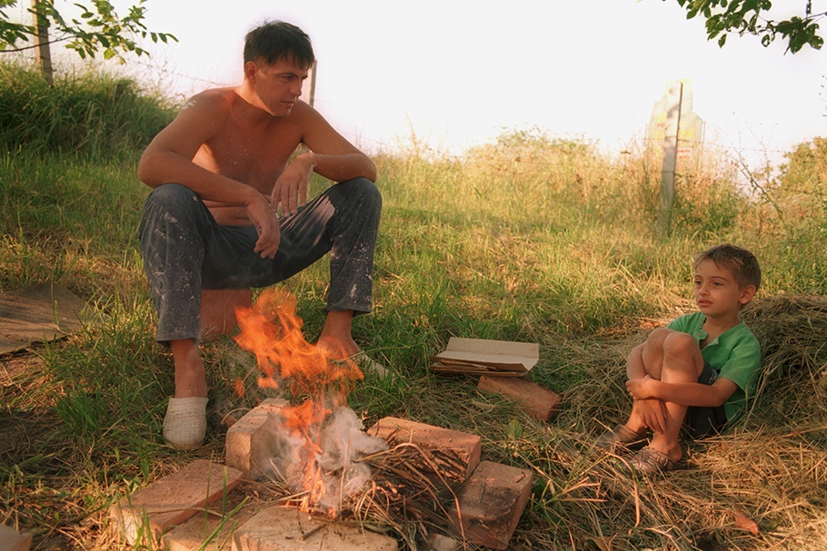 A father and son sit by a fire.