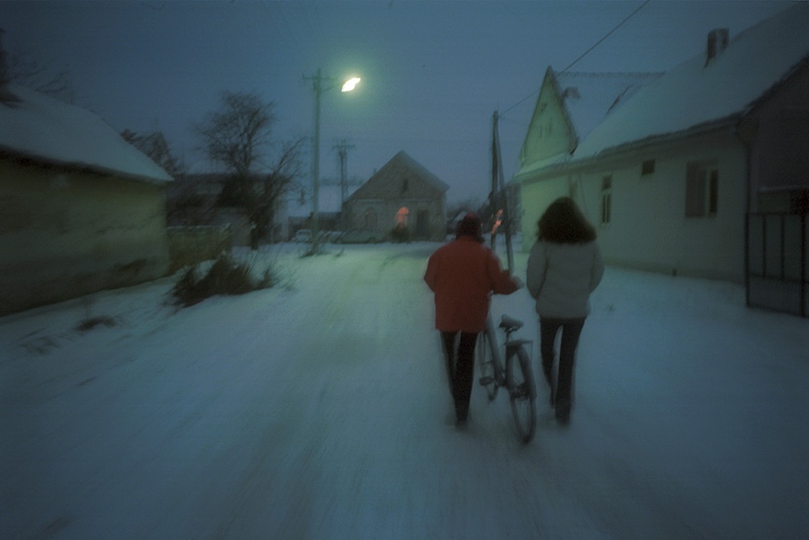 Two women walk down a snowy street at night.