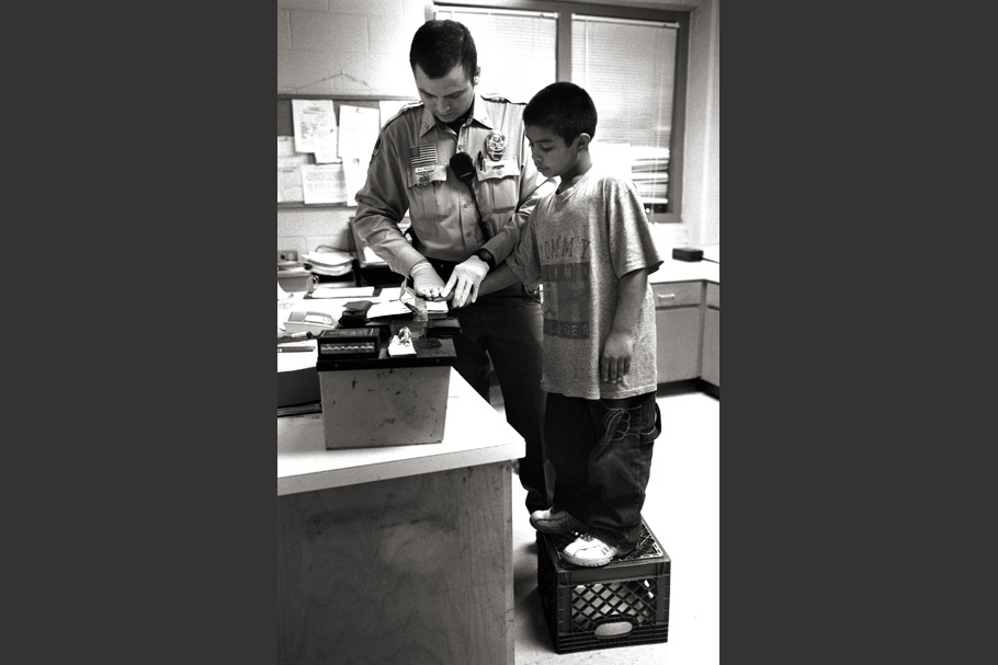 A boy is fingerprinted while standing on a milk crate.