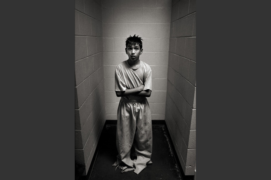A boy in a cell wearing clothes that are too large.