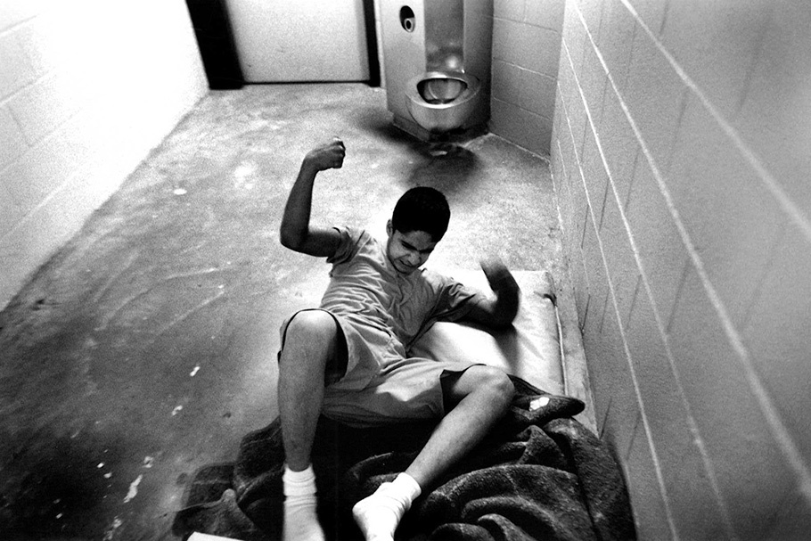 A boy thrashes around on the floor of a cell.