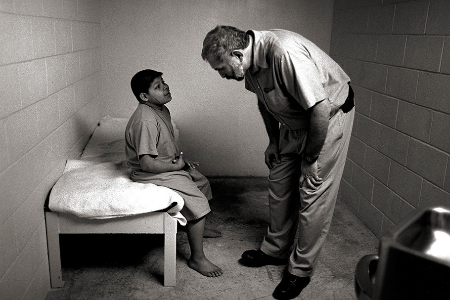 Guard talking to a young boy in a cell.