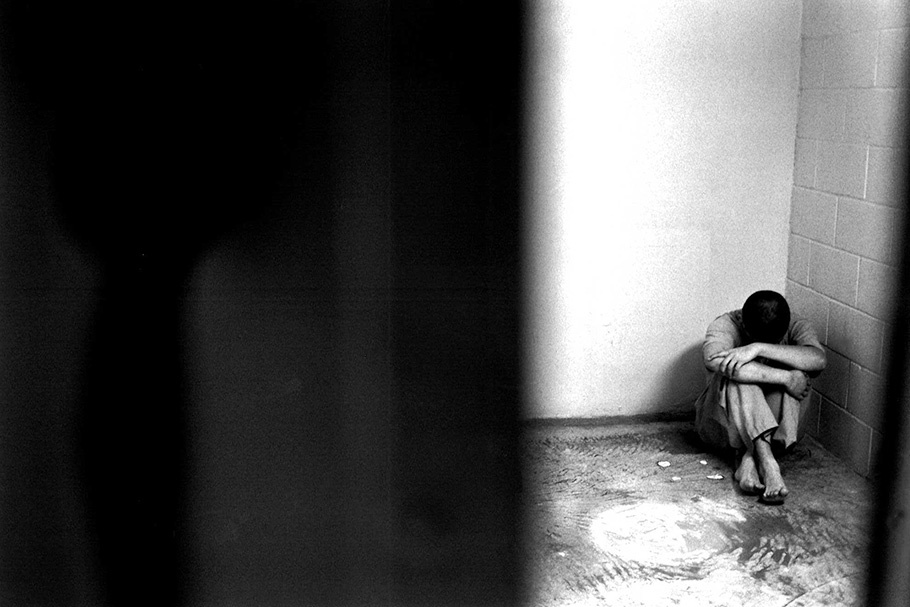 A boy curled up on the floor of a cell.
