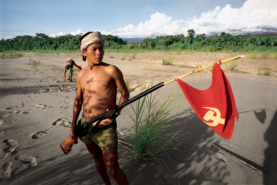 A young man holding a gun with a red flag. 