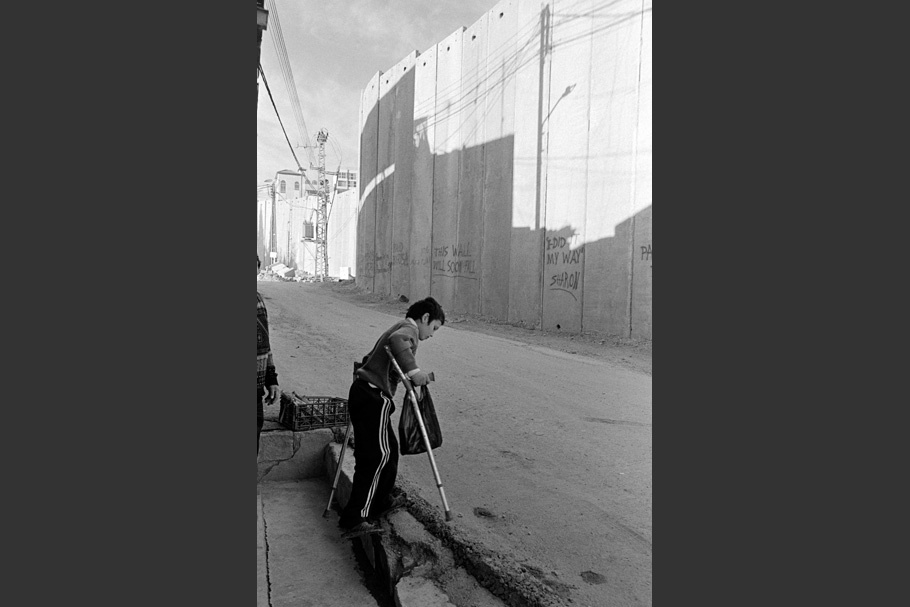 A boy with crutches walking near the wall.