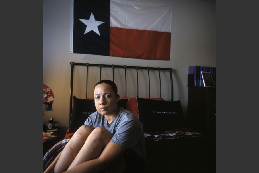 Female soldier sitting on bed under Texan flag.