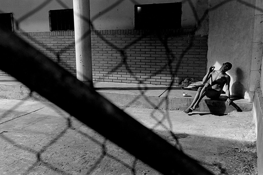 A patient, viewed through bent chicken wire, sitting in the sun.