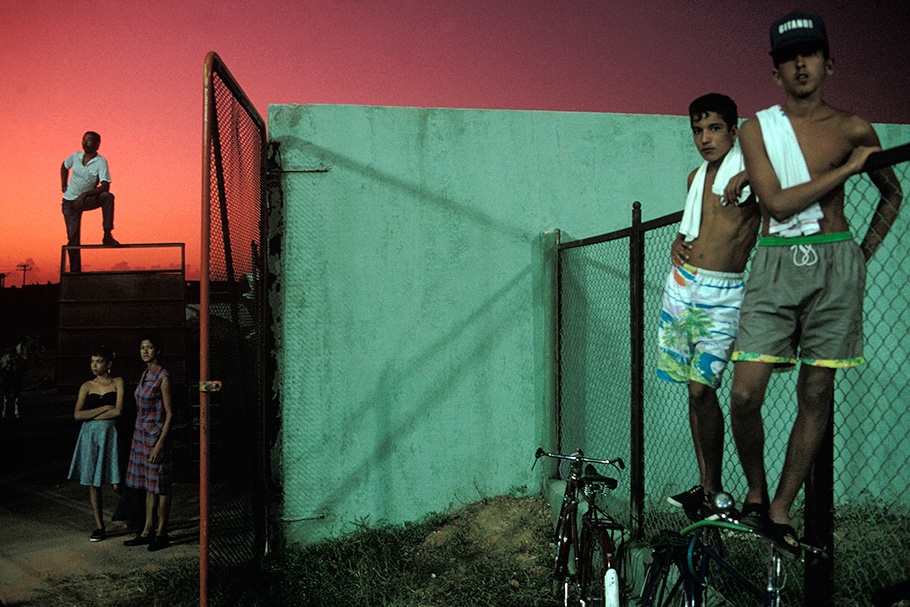 Five teens with a fence, a wall, bikes, and a red sky.
