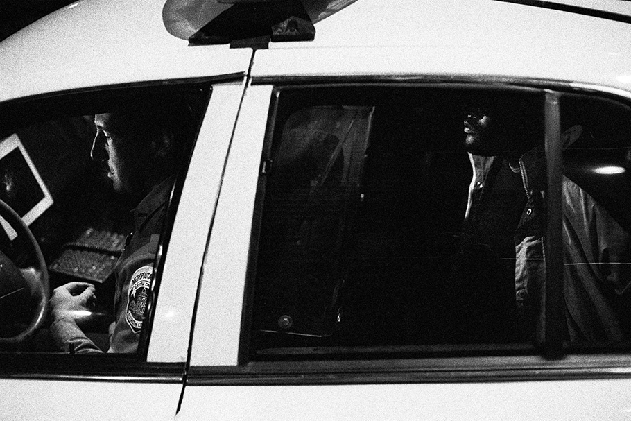 Officer and man seen through the side of a police car.