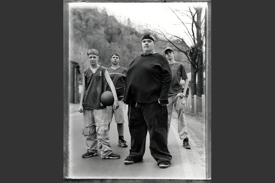 Four teenage boys standing in a road, one with a basketball.