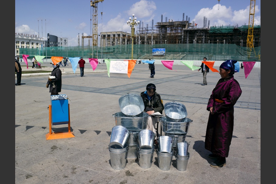 Women selling tin buckets under a string of flags.