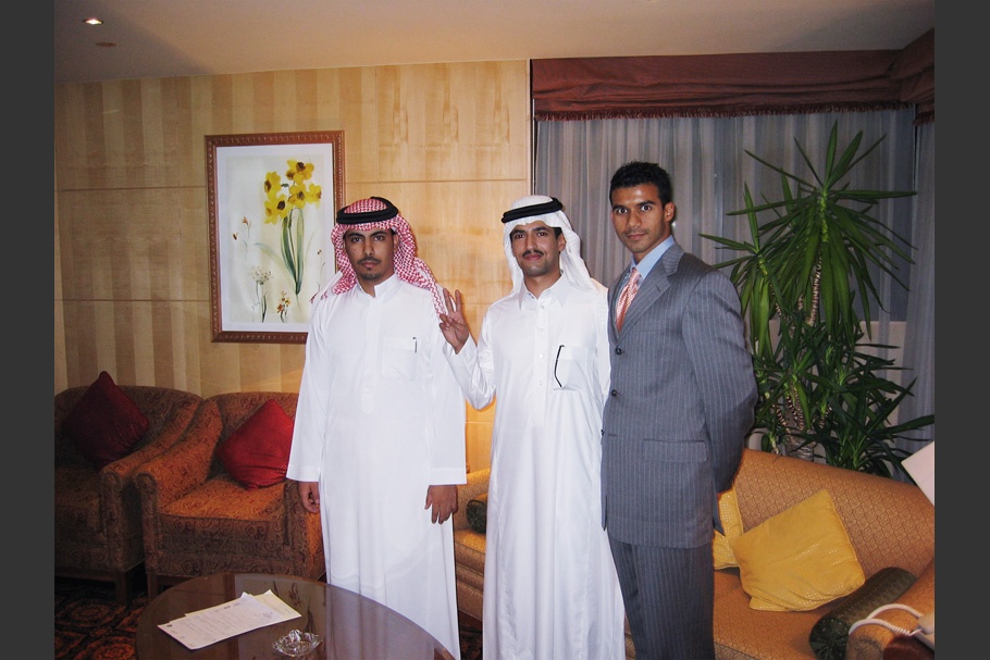 Portrait of three men, two in white with headscarves, one in a suit.
