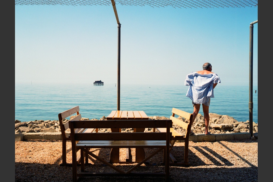Man and table in front of water, blue shirt.