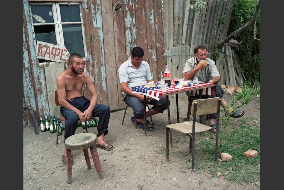 Three men sitting at a table with an American flag on it.
