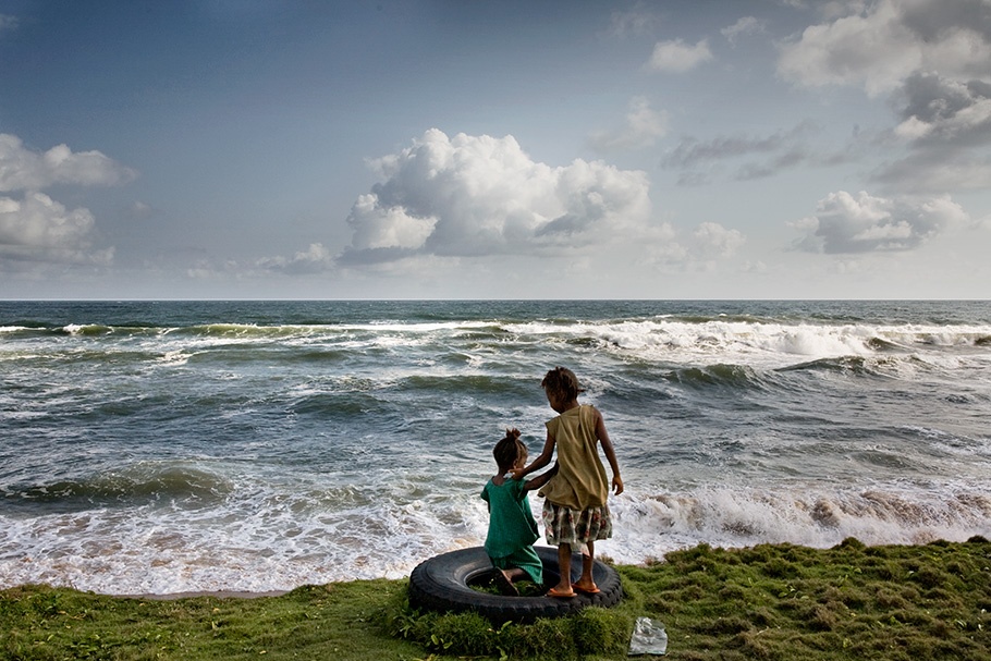 Children playing on tire in front of ocean.