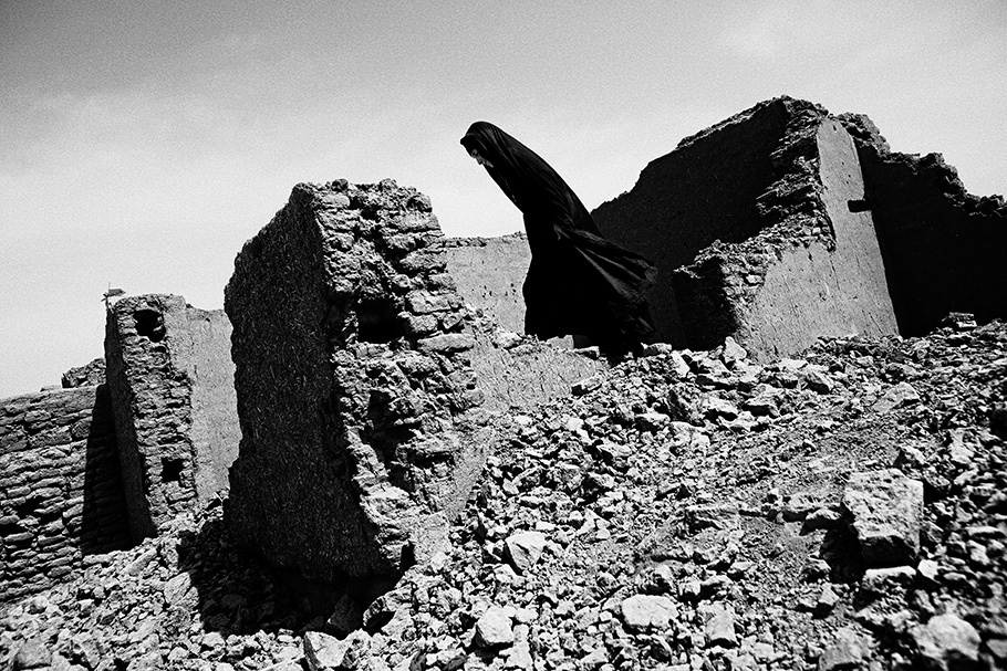 Woman in black walking through ruined building.