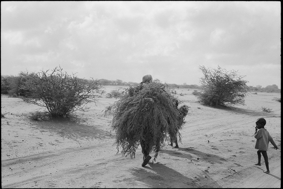 Woman carrying thatch with a child on the right.