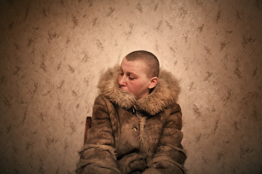 A woman with a shaved head sits in a chair.