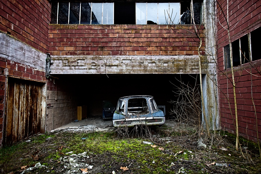 Abandoned car parked outside an abandoned factory building. 