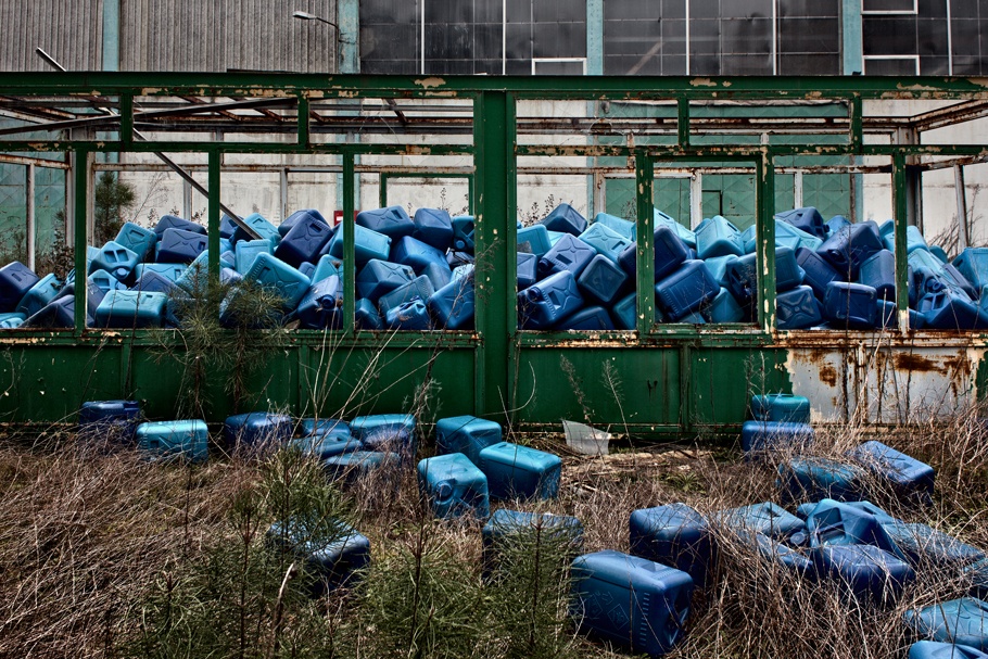 Blue plastic containers piled outside an abandoned factory. 