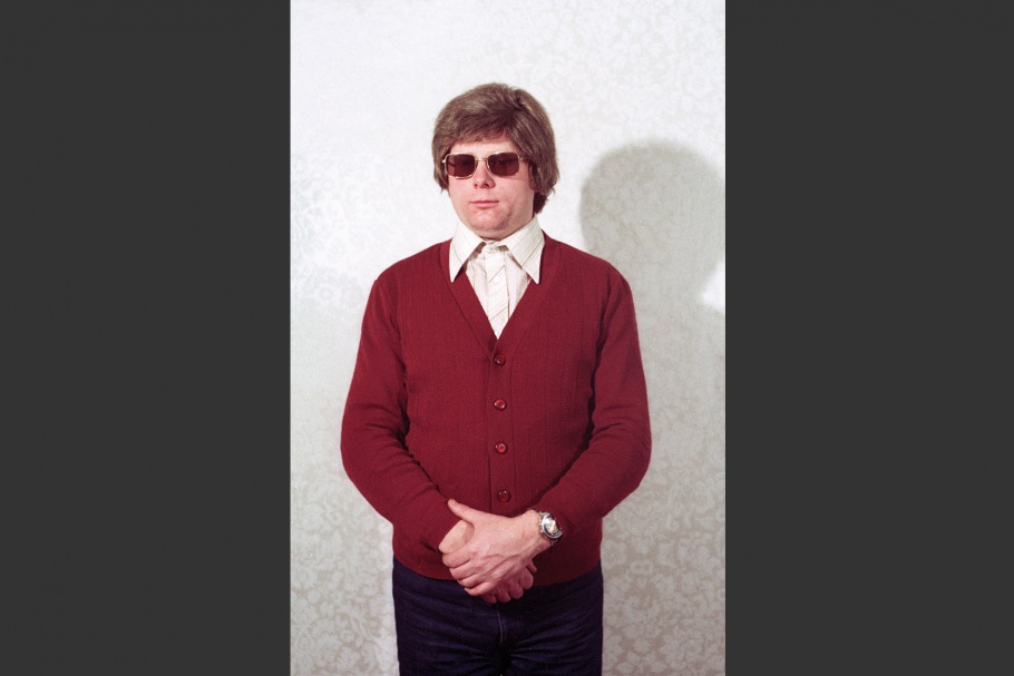 Man with maroon cardigan and sunglasses, hands held in front