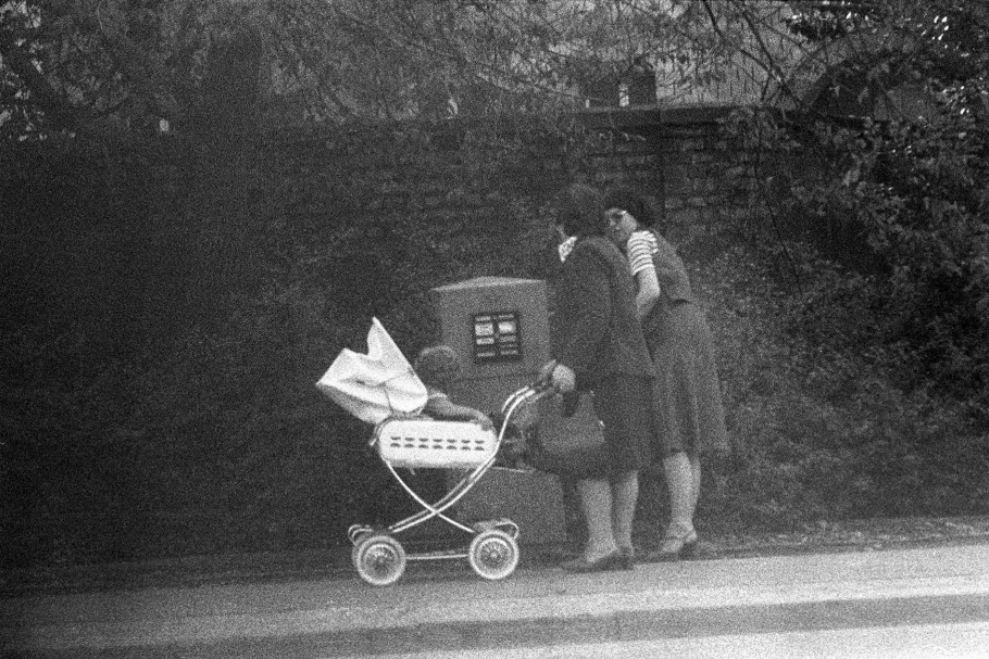 Two women, one pushing baby carriage, in front of mailbox