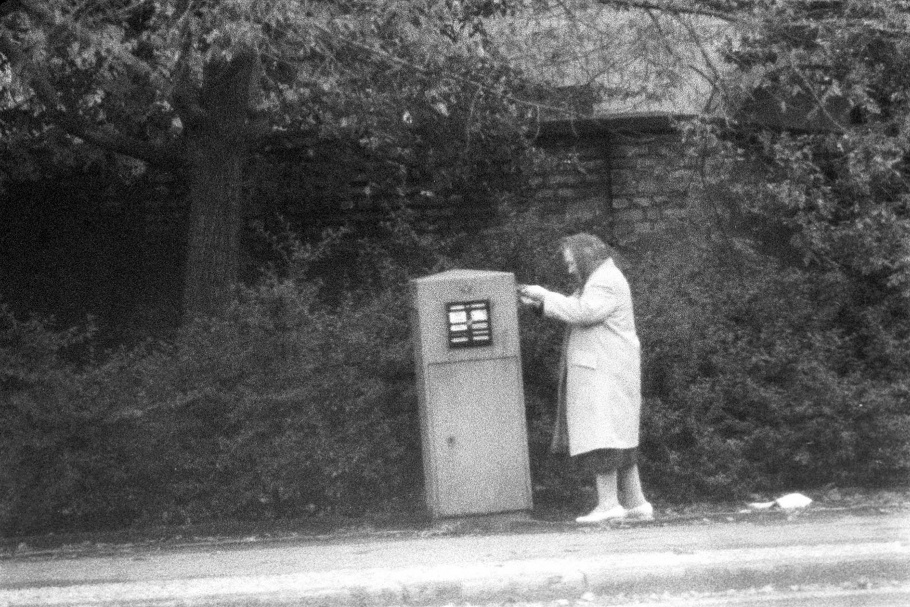 Elderly woman with scarf covering head, placing mail in mailbox