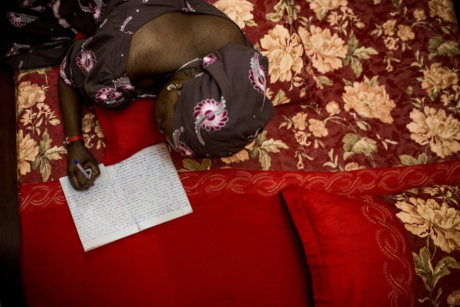 A Nigerian romance novelist writes while lying on a red bed