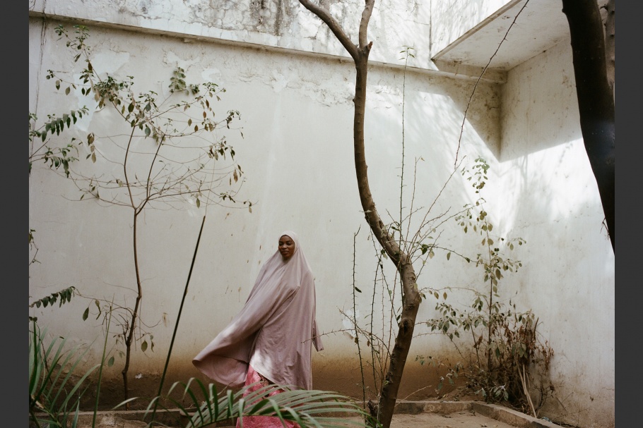 A Nigerian romance novelist wearing pink walks in a courtyard
