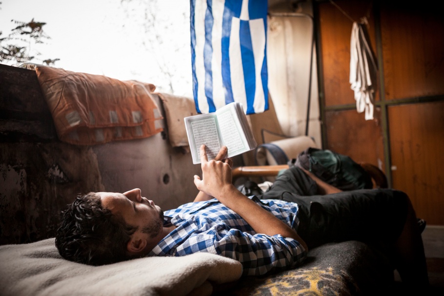 A man reads the Koran beneath a Greek flag