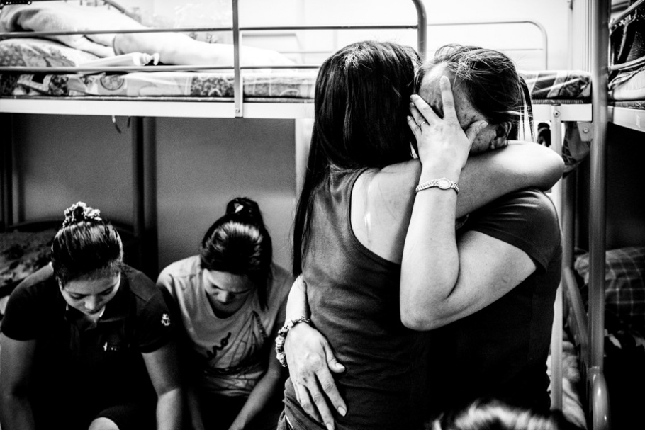 A woman covering her face while being hugged by another woman.