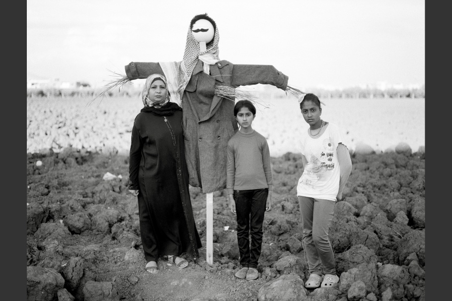 A woman and two girls stand next to a scarecrow