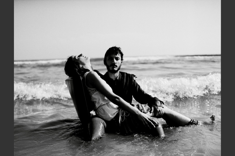 A man on a beach sitting in the water holding a woman on his lap
