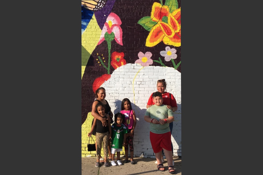 Two women and children posing in front of a mural