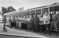 Twelve men in chains in front of a bus with two guards.