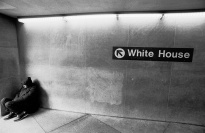 A homeless man in a corridor with a “White House” sign.
